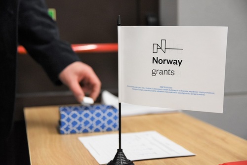 Na pierwszym planie widać chorągiew Norweskiego Mechanizmu Finansowania, w tle uczestnicy losują numer miejsca