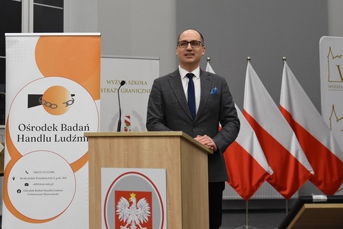 Przewodniczący egzaminu końcowego wita funkcjonariuszy-studentów na tle banerów i biało-czerwonych flag