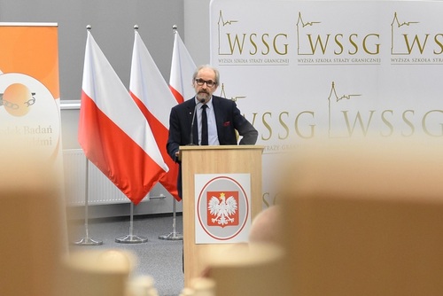 Prof. dr hab. Zbigniew Lasocik – Kierownik Ośrodka Badań Handlu Ludźmi UW przemawia na tle banerów i biało-czerwonych flag