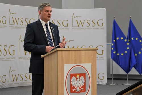 Płk SG Piotr Rosłaniec – Dyrektor Zarządu Operacyjno-Śledczego KGSG podczas przemówienia. W tle baner WSSG oraz flagi Unii Europejskiej