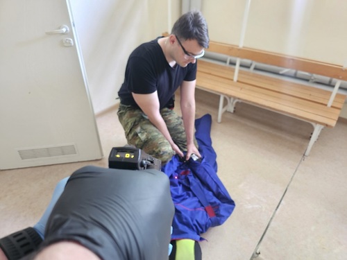 Trzymany w dłoniach paralizator z wiązką światła skierowana na plecy pozoranta, drugi funkcjonariusz obezwładnia pozoranta Trzymany w dłoniach paralizator z wiązką światła skierowana na plecy pozoranta, drugi funkcjonariusz obezwładnia pozoranta