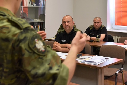 Fragment umundurowania, na drugim planie siedzący uczestnicy kursu Fragment umundurowania, na drugim planie siedzący uczestnicy kursu