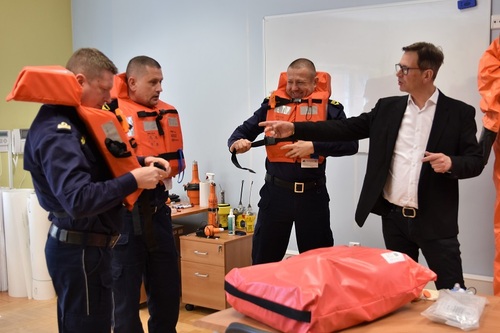 Kursanci mający na sobie kamizelki ratunkowe, wykładowca gestykuluje Kursanci mający na sobie kamizelki ratunkowe, wykładowca gestykuluje